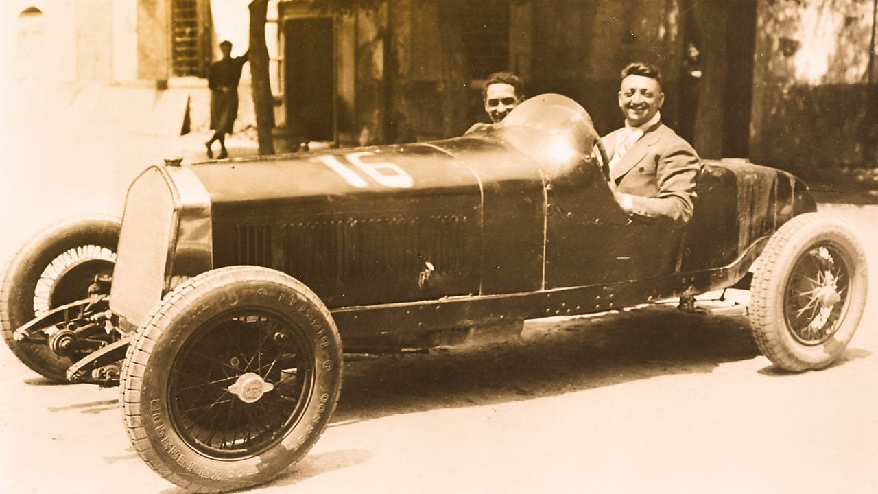 Black and white photo of Enzo Ferrari sitting in one of the first Ferrari cars