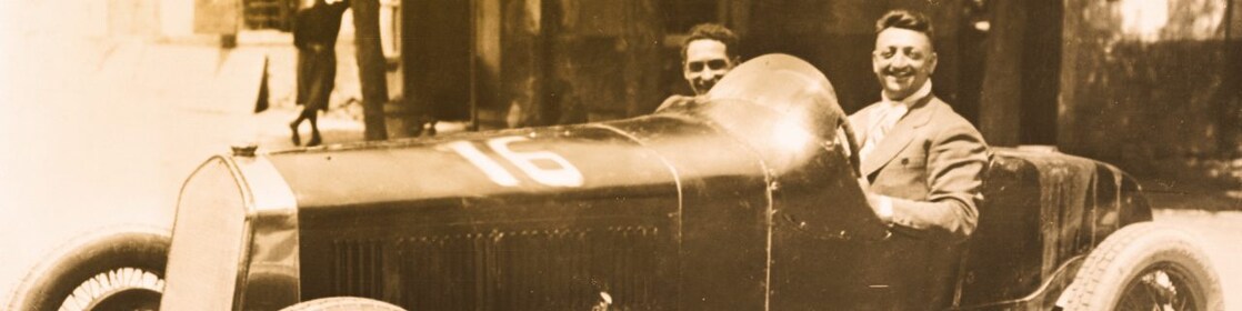 Black and white photo of Enzo Ferrari sitting in one of the first Ferrari cars