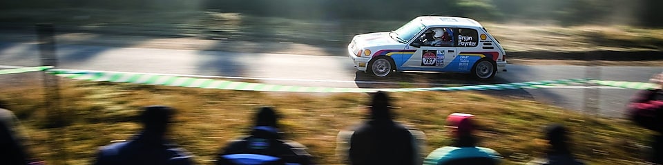 Rally car driving along a road in front of a crowd of spectators