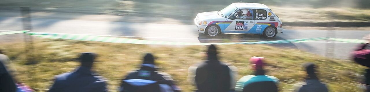 Rally car driving along a road in front of a crowd of spectators