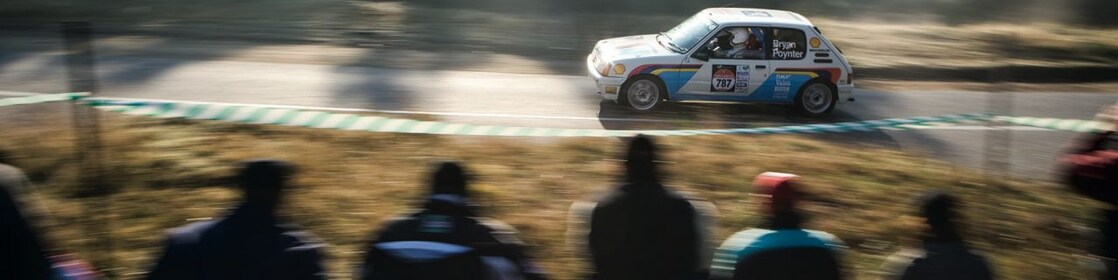 Rally car driving along a road in front of a crowd of spectators