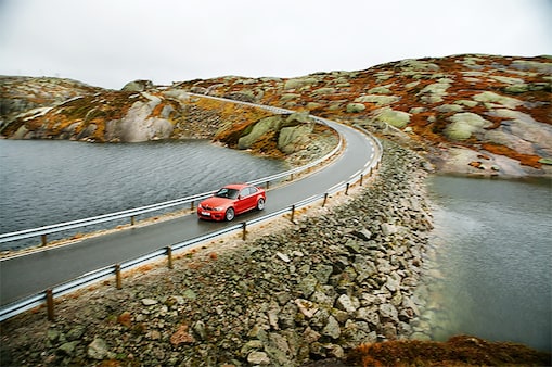 Red coloured car on a riverside road