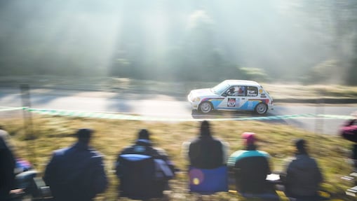 Rally car driving along a road in front of a crowd of spectators