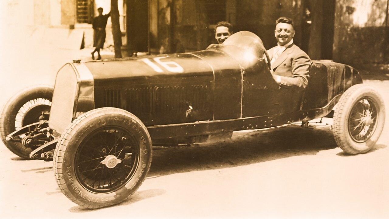 Black and white photo of Enzo Ferrari sitting in one of the first Ferrari cars