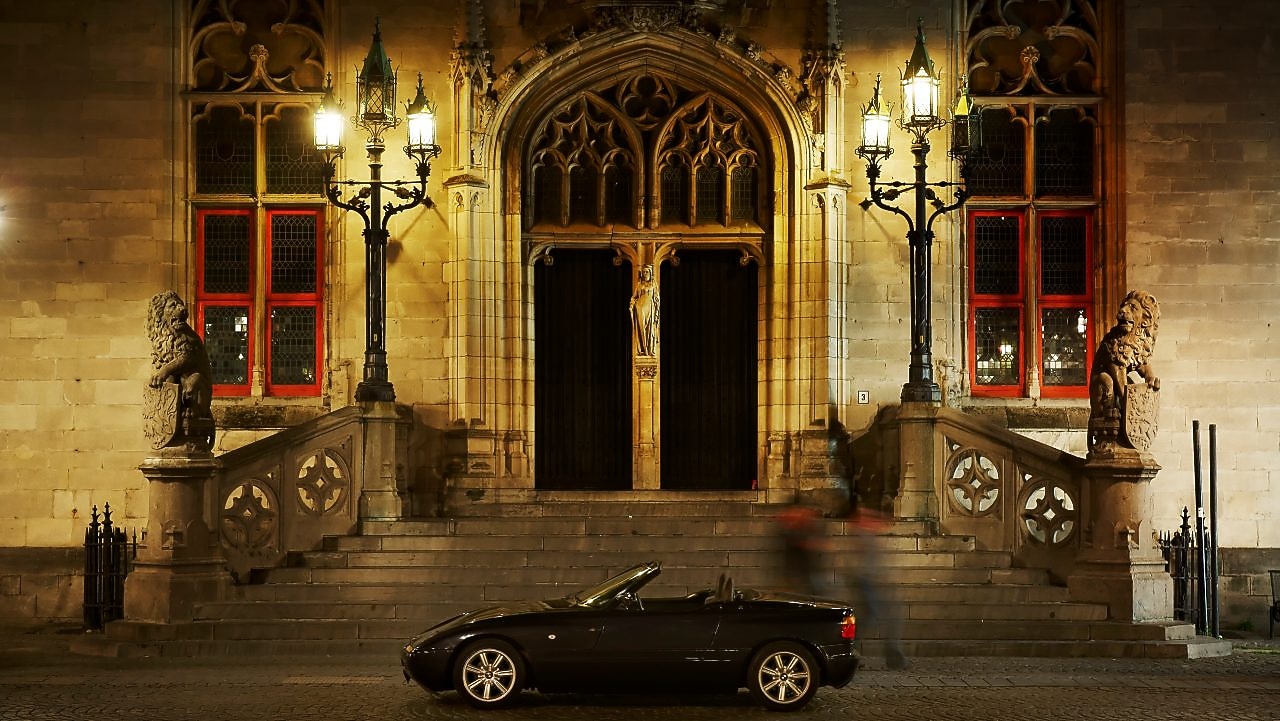 Black car parked outside of a large house at night, next to some stone steps