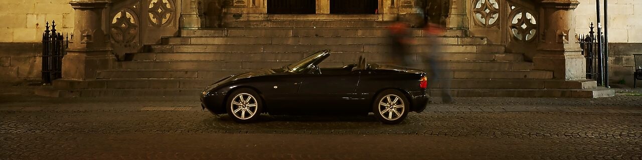 Black car parked outside of a large house at night, next to some stone steps