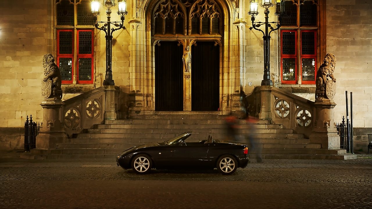 Black car parked outside of a large house at night, next to some stone steps