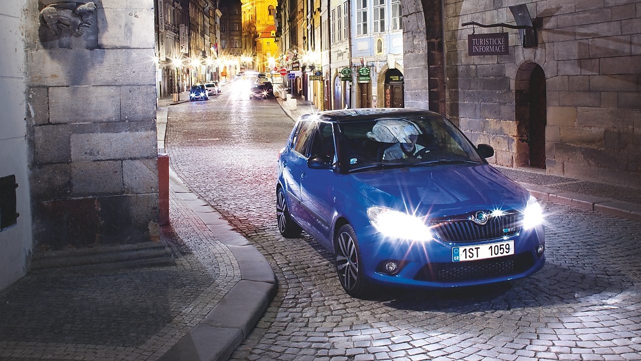 Blue car parked under an arch on a cobbled Prague road at night