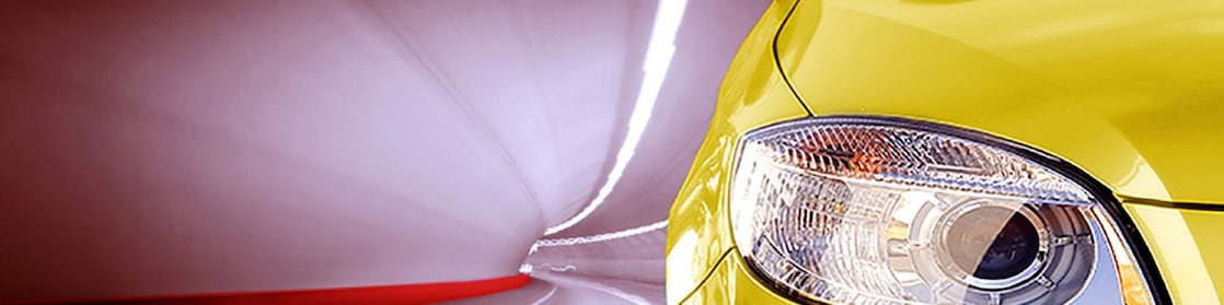 Front of a yellow car driving through a tunnel, right front light and wing mirror in view