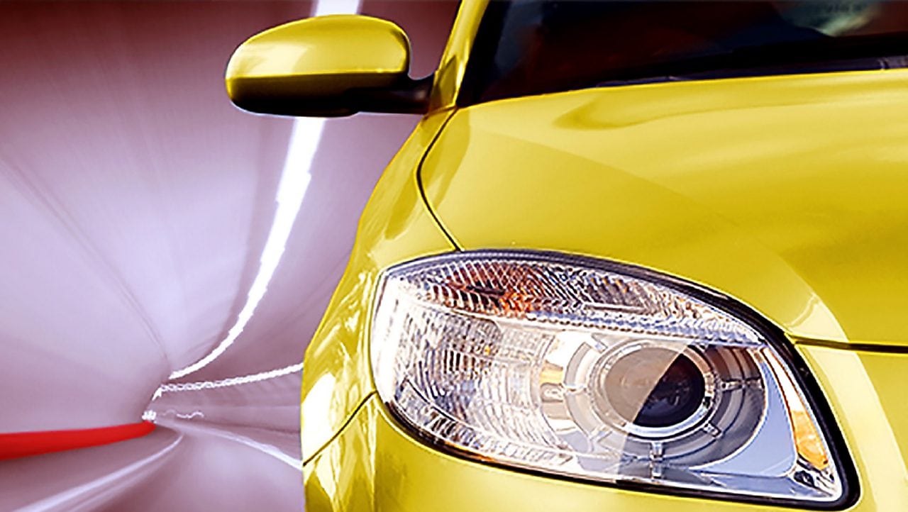 Front of a yellow car driving through a tunnel, right front light and wing mirror in view