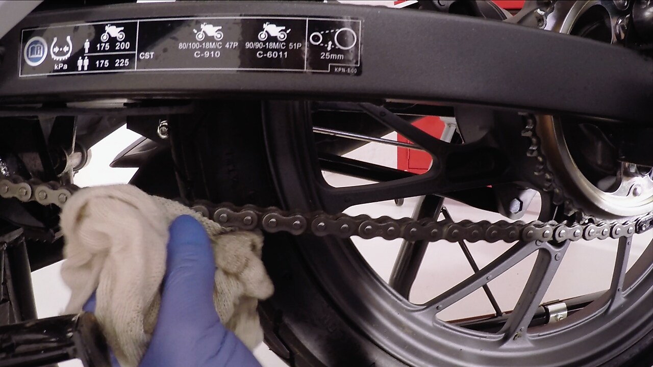 hands removing excess lubricant on a motrocycle chain