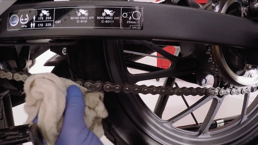 hands removing excess lubricant on a motrocycle chain