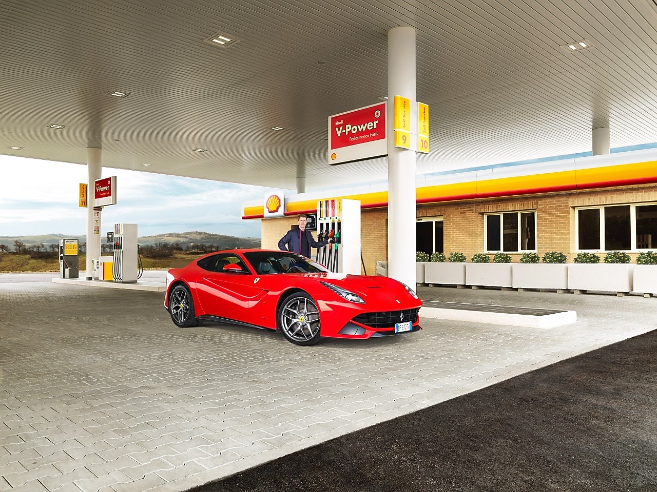 A red Ferrari sitting on a Shell station forecourt with a man leaning on a petrol pump